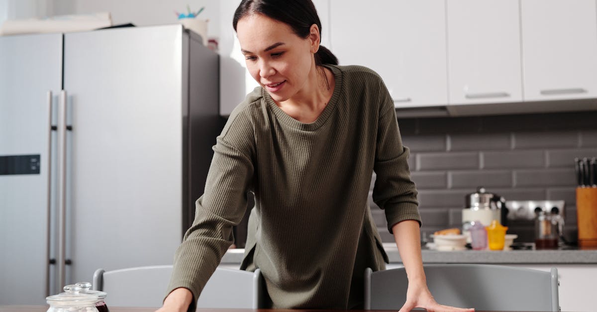 Woman cleaning a kitchen table with a cloth in a modern kitchen setting, maintaining hygiene.